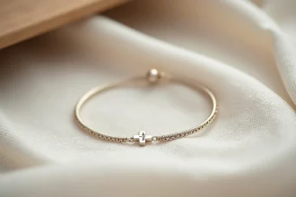 Bracelet de baptême en or blanc avec croix gravée posé sur tissu lin ivoire, vue macro dans un atelier de joaillerie